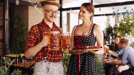 Man-and-woman-in-traditional-clothes-standing-with-lager-beer-and-appetizers-at-pub.-Serving-beer-to-group-of-friends.-Concept-of-oktoberfest,-traditional-taste,-friendship,-leisure-time,-enjoyment