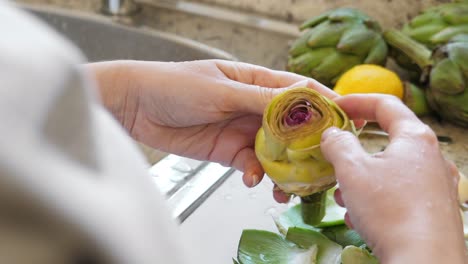 Woman-peeling-artichokes.-Cooking-process-at-modern-kitchen