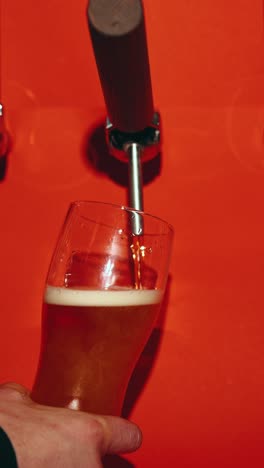 Bartender-slowly-pouring-delicious-lager-foamy-beer-in-glass-against-red-background.-Close-up-of-bubbles.-Concept-of-drink,-brewery,-taste,-bar,-degustation,-festival,-drink-texture.-Vertical-layout