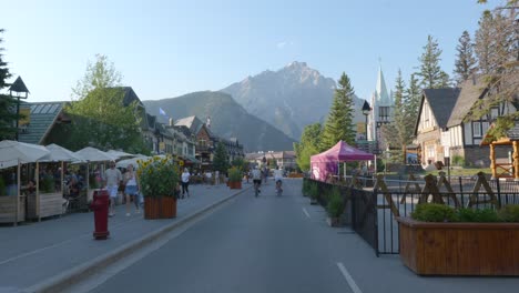 Menschen,-Die-An-Einem-Sonnigen-Tag-Auf-Der-Banff-Avenue-Mit-Bergen-Im-Hintergrund-Rad-Fahren