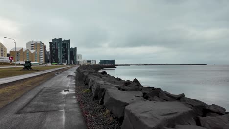 Una-Toma-Panorámica-De-La-Costa-De-Reykjavik-Muestra-Un-Camino-Pavimentado-Y-Edificios,-Incluidos-Altos-Edificios-De-Apartamentos.