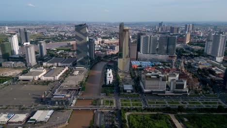 Aerial-view-of-Phnom-Penh-government-buildings,-city-skyline,-skyscrapers-across-Twin-Dragon-bridge-on-Tonle-sap-river