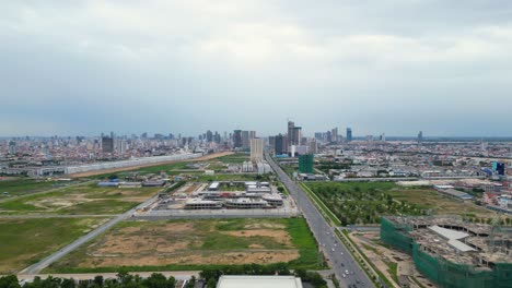 Aerial-view-of-Phnom-Penh,-Cambodia’s-busy-capital,-drone-approaching-modern-skyline-skyscraper-building-at-distance