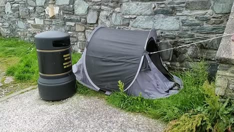 Abandoned-homeless-persons-camping-tent-alongside-council-trash-bin-in-Welsh-seaside-town-sidewalk