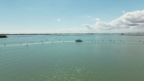 Ruhige-Luftaufnahmen-Eines-Bootes,-Das-Unter-Einem-Klaren-Blauen-Himmel-Durch-Die-Ruhigen-Gewässer-Der-Lagune-Von-Venedig-Navigiert