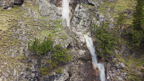 Vista-Aérea-De-Cascadas-Gemelas-Que-Caen-En-Cascada-Por-Acantilados-Rocosos-En-Las-Montañas-Dolomitas,-Rodeadas-De-Un-Bosque-Verde.