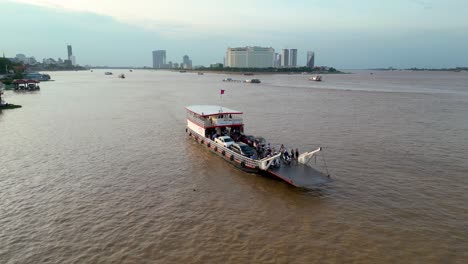 Drohnenaufnahme-Eines-Fährdienstes,-Der-Passagiere-Und-Fahrzeuge-Auf-Dem-Mekong-Transportiert,-Mit-Blick-Auf-Das-Sokha-Hotel