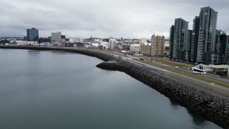 Eine-Luftaufnahme-Von-Reykjavik-Zeigt-Die-Skyline-Der-Stadt-Mit-Modernen-Und-Traditionellen-Gebäuden-Und-Einer-Felsigen-Ufermauer