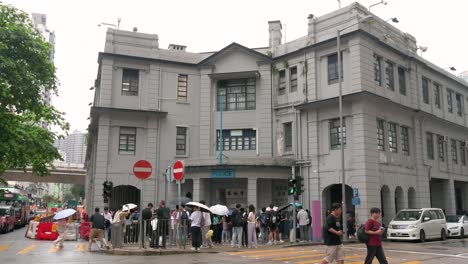 On-a-rainy-day,-crowds-of-Chinese-tourists-gather-in-front-of-the-former-Yau-Ma-Tei-Police-Station,-a-popular-tourist-spot-featured-in-many-Hong-Kong-films-and-TV-shows