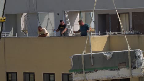 Un-Enorme-Bloque-De-Hormigón-Que-Desciende-Es-Seguido-Y-Supervisado-Por-Trabajadores-De-La-Construcción-Durante-La-Renovación-De-Una-Casa-En-Marsaskala,-Malta