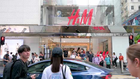 Chinese-pedestrians-wait-at-a-traffic-light-on-a-busy-street-just-outside-the-H-and-M-store-in-Hong-Kong,-a-symbol-of-international-fashion