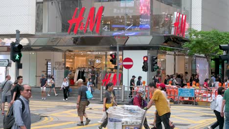 In-front-of-the-Swedish-retail-giant-H-and-M-in-Hong-Kong,-Chinese-pedestrians-cross-the-street,-highlighting-the-city's-vibrant-urban-life