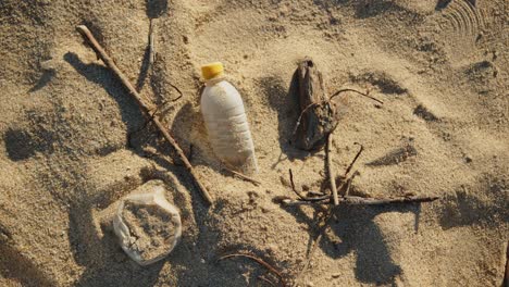 Plastic-bottle-on-a-beach-with-small-tree-sticks,-Pollution