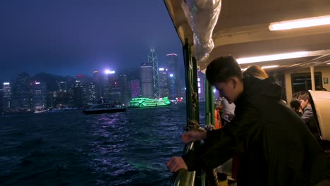 Chinese-visitors-take-a-nighttime-ride-on-the-Star-Ferry,-enjoying-views-of-the-landmark-Hong-Kong-skyline