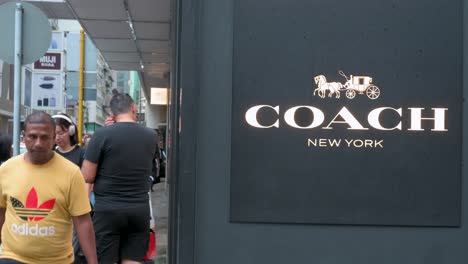 Fußgänger-Gehen-An-Der-Amerikanischen-Multinationalen-Mode--Und-Luxus-Accessoire-Kette,-Dem-Coach-Geschäft-Und-Dem-Logo-In-Hongkong-Vorbei