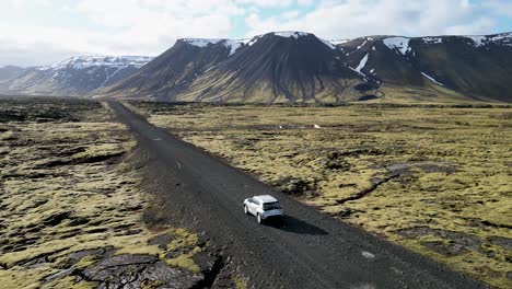 Conduciendo-Por-Islandia,-Un-Todoterreno-Recorre-Un-Camino-De-Grava-A-Través-De-Montañas-Y-Paisajes-Cubiertos-De-Musgo.