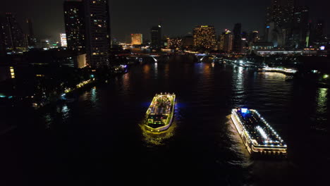 AERIAL:-Backwards-in-front-of-a-ferry-on-the-Chao-Phraya-River,-night-in-Bangkok