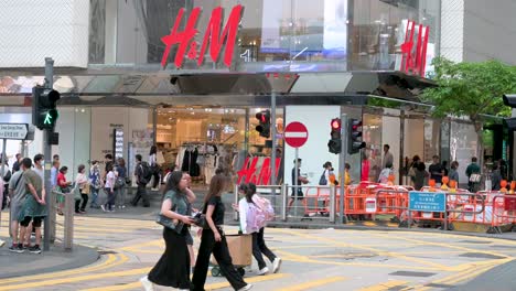 Chinese-pedestrians-cross-the-street-in-front-of-the-Swedish-multinational-clothing-design-retail-company-Hennes-and-Mauritz,-H-and-M,-store-in-Hong-Kong