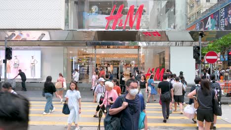 In-Hong-Kong,-pedestrians-cross-the-street-in-front-of-the-prominent-H-and-M-store,-a-well-known-Swedish-clothing-design-retail-company