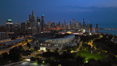 AERIAL:-Illuminated-Soldier-field-stadium-and-the-Field-Museum,-dusk-in-Chicago