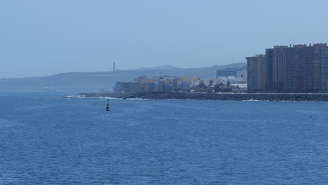 Coastal-view-of-Gran-Canaria-with-urban-buildings-along-the-shoreline-and-mountains-in-the-background,-seen-from-the-ocean