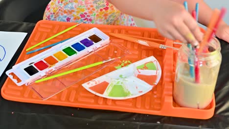 child-cleaning-a-paintbrush-in-water-on-an-art-pad