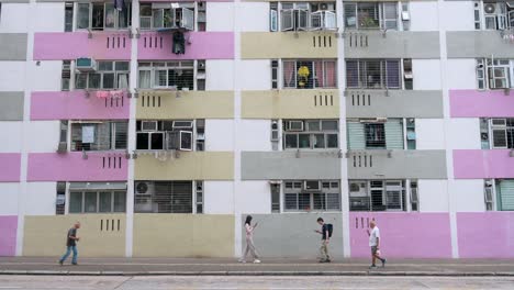 Los-Residentes-Caminan-Por-La-Calle-Junto-A-Un-Edificio-De-Viviendas-Públicas-De-Gran-Altura-Y-Colores-Brillantes-En-Hong-Kong.