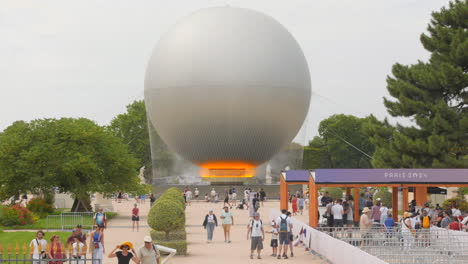 Visitors-gather-in-Tuileries-Gardens-to-admire-the-radiant-Olympic-cauldron-surrounded-by-lush-greenery-and-vibrant-sculptures