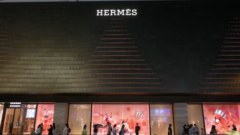 Pedestrians-walk-past-the-French-high-fashion-luxury-clothing-manufacturer-Hermes-store-during-nighttime