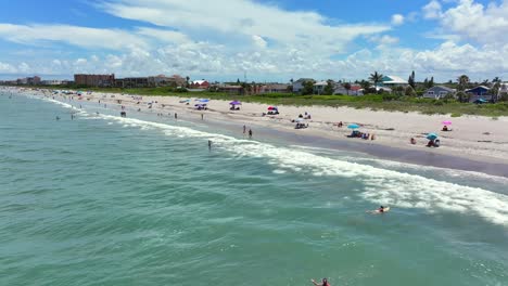 Küste-Von-Cape-Canaveral-Mit-Sonnenanbetern-Unter-Bunten-Sonnenschirmen-Und-Schwimmern,-Die-Die-Wellen-Des-Atlantiks-Genießen