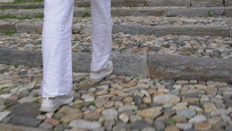 Mujer-Con-Pantalones-Blancos-Subiendo-Escaleras-De-Una-Calle-Adoquinada-En-Italia