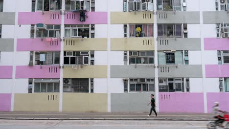 Escena-Callejera-Que-Muestra-A-Personas-Caminando-Frente-A-Un-Edificio-De-Viviendas-Públicas-De-Gran-Altura-Pintado-De-Colores-Vivos-En-Hong-Kong