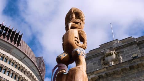 Close-up-of-Maori-Te-Kāhui-Mōuri-taonga-statue-at-Parliament-building-with-Beehive-landmark-in-capital-city-of-Wellington-NZ-Aotearoa