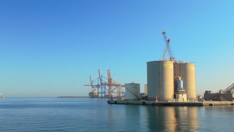 Malaga's-harbor-with-cranes-and-storage-tanks,-highlighting-the-bustling-industrial-activity-under-a-bright-blue-sky