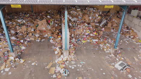 Paper-and-cardboard-waste-on-heaps-under-shelter-at-recycling-centre,-aerial