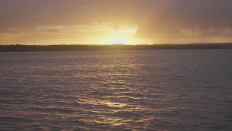 Ein-Atemberaubender-Sonnenuntergang-Von-Einem-Boot-Aus,-Der-Die-Letzten-Strahlen-Der-Orangefarbenen-Sonne-Mit-Vereinzelten-Wolken-Und-Langsamen-Wellen-Auf-Dem-Wasser-Einfängt-Und-So-Eine-Heitere-Und-Ruhige-Szene-Schafft