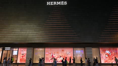 People-stroll-by-the-illuminated-Hermes-luxury-fashion-boutique-at-night