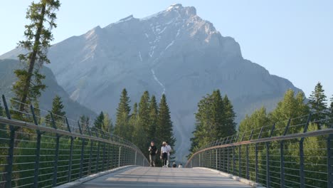 Personas-Caminando-Por-Un-Puente-Peatonal-Con-Impresionantes-Vistas-A-Las-Montañas-En-Banff,-Canadá