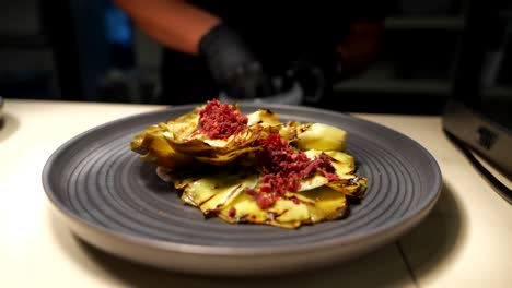 Chef-garnishing-artichokes-with-vibrant-ham-topping-in-modern-kitchen