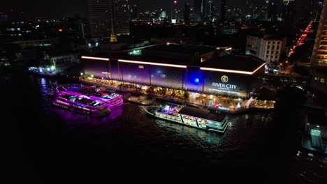 Vista-Aérea-De-Los-Transbordadores-En-La-Ciudad-Iluminada-Del-Río,-De-Noche-En-Bangkok