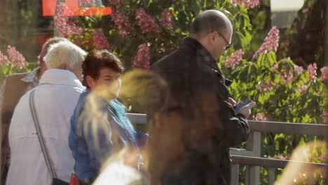 People-standing-by-a-railing-on-a-sunny-day,-reflections-in-glass