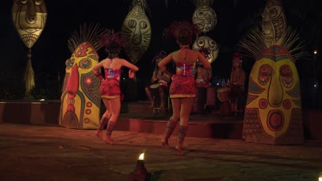 Colorful-traditional-Balinese-dance-performance-by-dancers-in-vibrant-costumes-with-mask-shields-lifted-as-they-wave-hands-and-hop