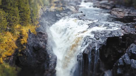 Scenic-overhead-shot-of-a-waterfall-flowing-forcefully-over-rocks,-surrounded-by-lush-greenery