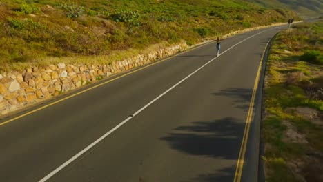 Toma-Aérea-Con-Dron-FPV-Hacia-Una-Niña-Que-Camina-Por-Una-Carretera-Costera-Durante-El-Atardecer