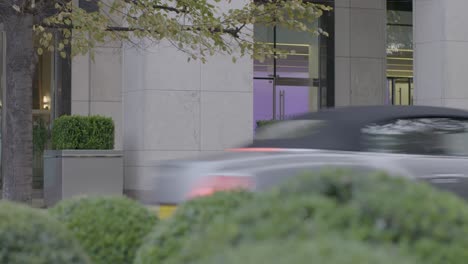 Modern-office-building-entrance-with-green-bushes-and-a-passing-car-in-the-foreground