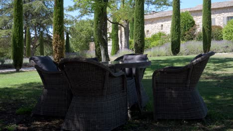 Una-Mesa-Redonda-Con-Tapa-De-Vidrio-Ocupa-Un-Lugar-Central-En-Un-área-De-Asientos-Al-Aire-Libre-Ubicada-Dentro-De-Un-Exuberante-Jardín-Verde.