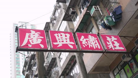 Un-Antiguo-Cartel-Publicitario-De-Un-Negocio,-Escrito-En-Caracteres-Chinos,-Cuelga-De-La-Fachada-De-Un-Edificio-En-Una-Calle-Residencial-En-La-Zona-De-Sham-Shui-Po-De-Kowloon,-Hong-Kong.