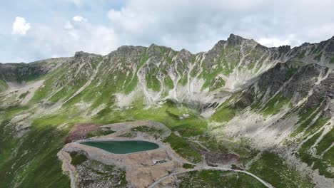 Epic-drone-backwards-shot-of-mountain-lake-with-rocky-mountain-range-and-moss-in-background