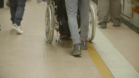 People-standing-in-line-at-a-train-station,-some-helping-person-in-a-wheelchair