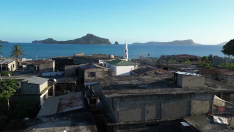 Drone-Volando-Sobre-Un-Pequeño-Pueblo-En-Mohéli-O-Mwali,-Parte-De-La-Unión-De-Las-Comoras,-Primer-Plano-Aéreo-De-La-Antigua-Mezquita-Blanca-De-Fomboni,-Patrimonio-árabe,-Con-Otras-Islas-Del-Archipiélago-Vistas-A-La-Distancia